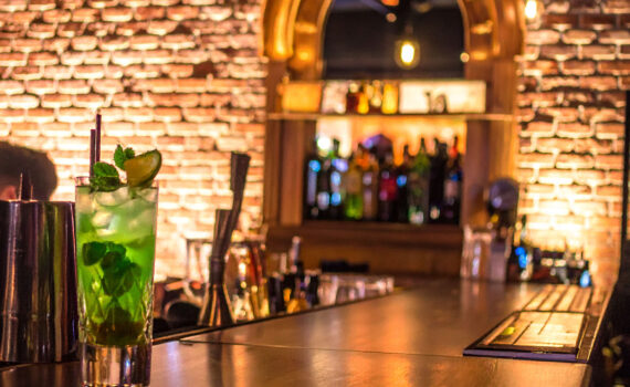 Eine stilvoll eingerichtete Bar mit beleuchteten Flaschen und Gläsern. Auf dem Tresen steht ein exklusiver Cocktail