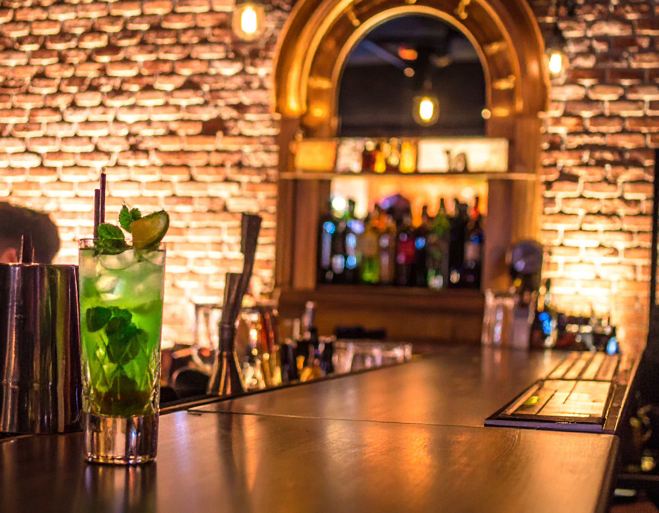 Eine stilvoll eingerichtete Bar mit beleuchteten Flaschen und Gläsern. Auf dem Tresen steht ein exklusiver Cocktail