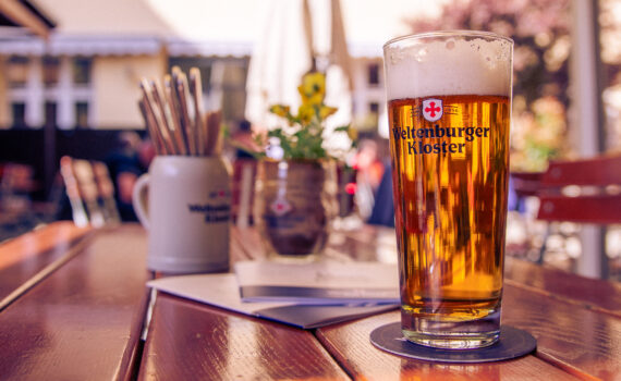Ein Glas frisch gezapftes Bier steht auf dem Tisch im Biergarten des Weltenburger am Dom
