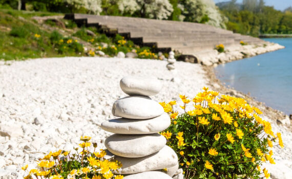 Ein sonniges Foto des Donaustrands in Schwabelweis. Im Vordergrund erstreckt sich ein Kiesstrand entlang des Ufers. Links davon befindet sich eine breite, gestufte Betontreppe, die zum Wasser hinabführt.
